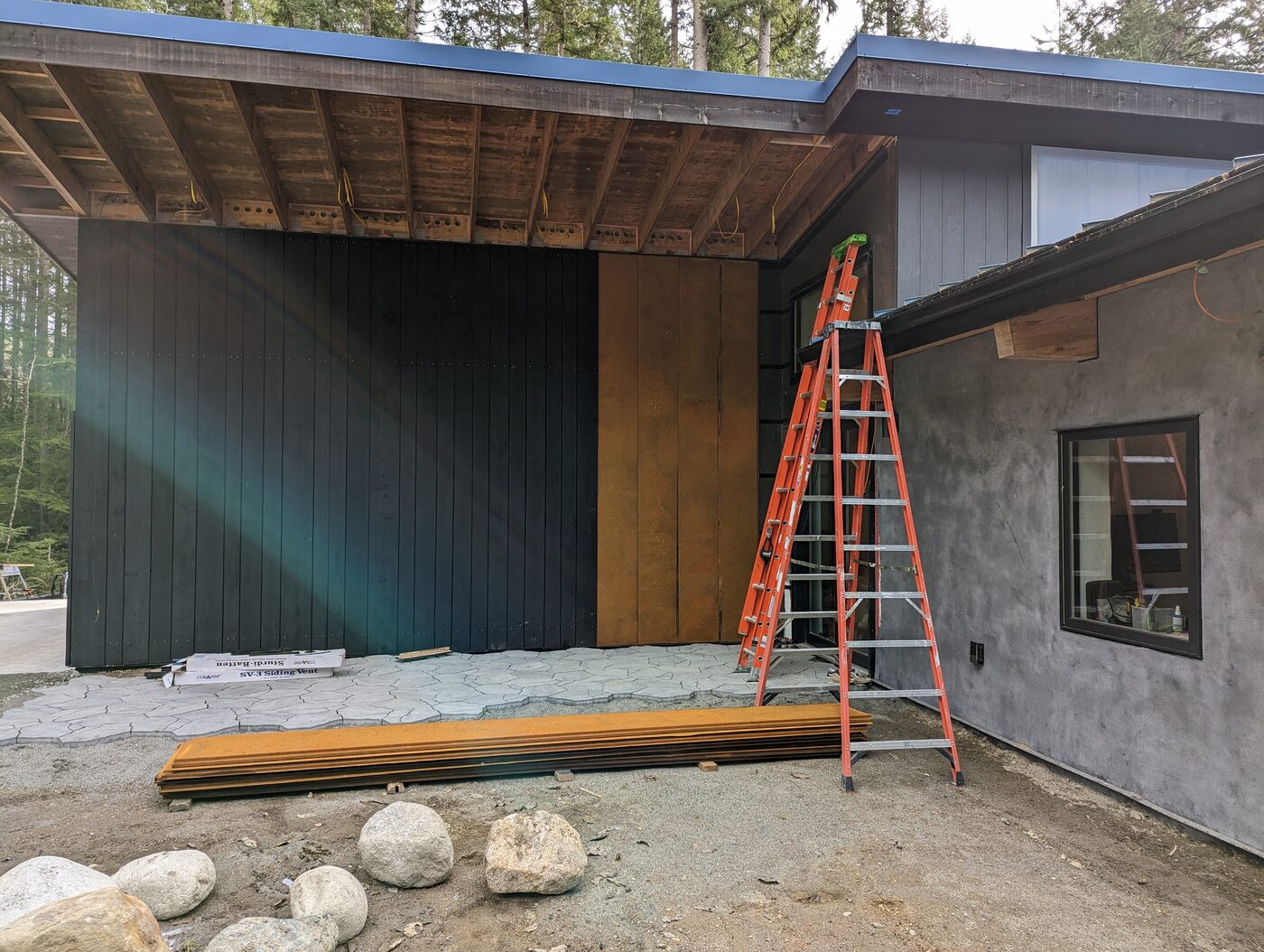 Fortress Foster exterior showing mixed materials — lime plaster stucco, shou sugi ban, and standing seam metal roof in the forest