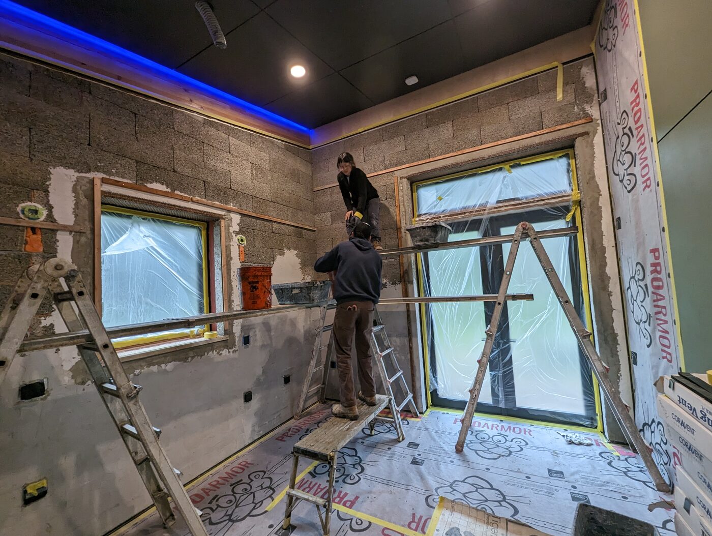Lime plaster being applied to Faswall ICF walls — two craftspeople working under blue accent lighting