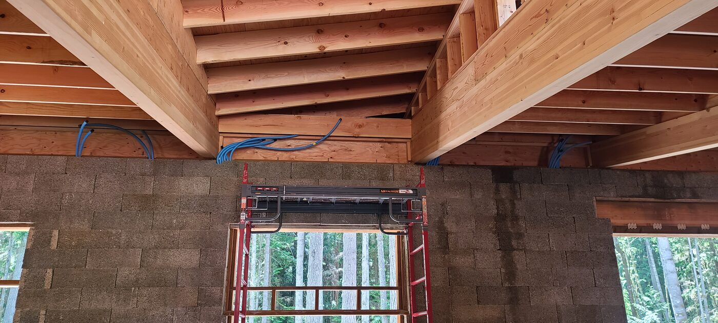 Timber beam-to-Faswall junction from inside — engineered lumber meeting ICF block walls with network cable routing above